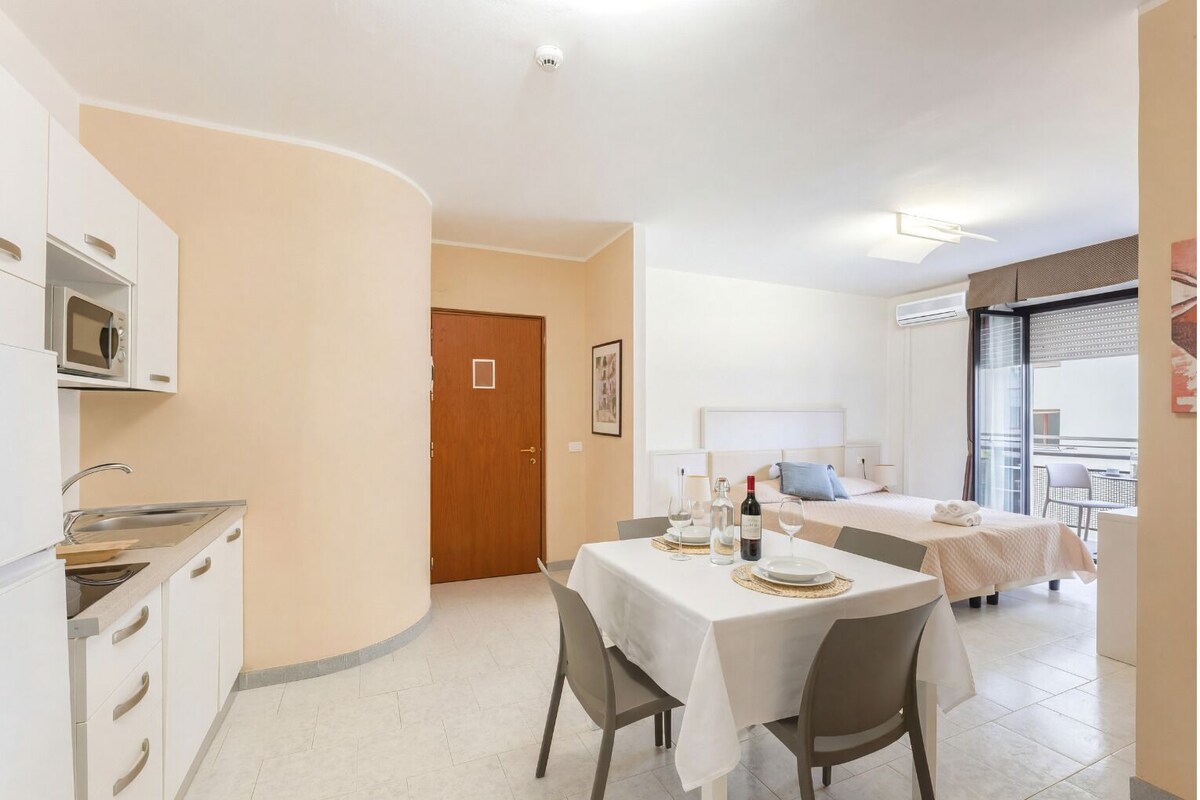 A compact hotel room with a kitchenette, a dining area, and a bed with a view.