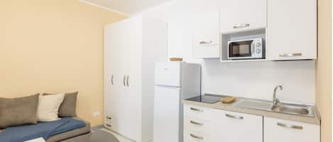 Una kitchenette compacta equipada con refrigerador, microondas y pileta. Hay un pequeño comedor con una mesa y una silla.