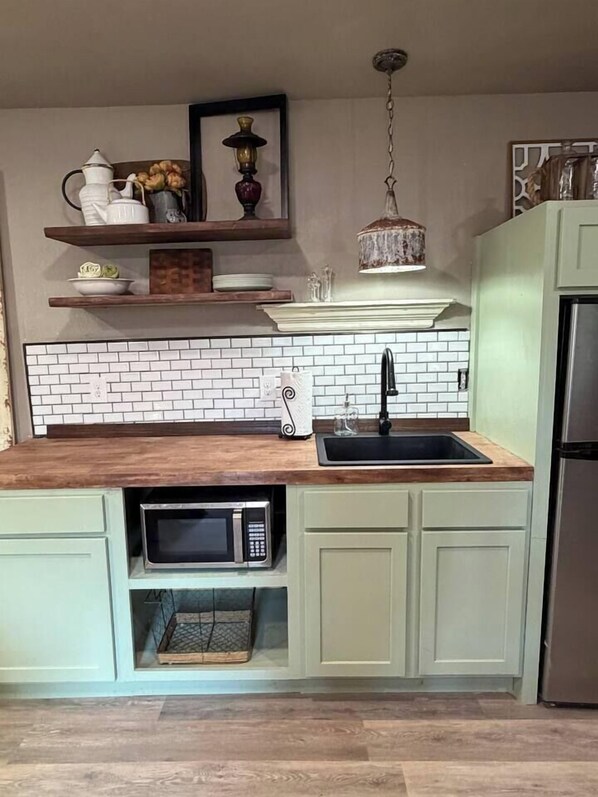 A kitchen with a wooden countertop, a stainless steel sink, a microwave, and a hanging light fixture.