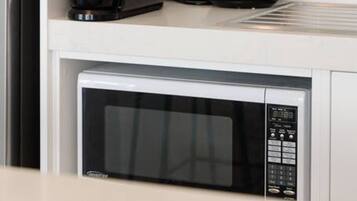 A kitchen with a stainless steel refrigerator, a black coffee maker, a white kettle, and a black microwave.