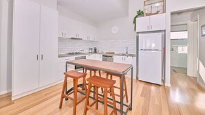 A modern kitchen with white cabinets, a wooden table, and two stools. - Grove Hideaway - immaculate 2 bed townhouse (Ocean Grove)