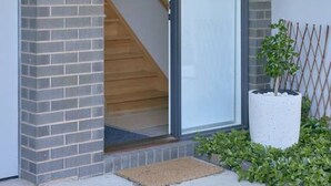 A modern building entrance with a glass door, a wooden staircase, and a potted plant. - Grove Hideaway - immaculate 2 bed townhouse (Ocean Grove)