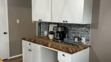 Cocina compacta con armarios blancos, encimera con motivo de espiga y cafetera.