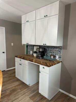 Cocina compacta con armarios blancos, encimera con motivo de espiga y cafetera.