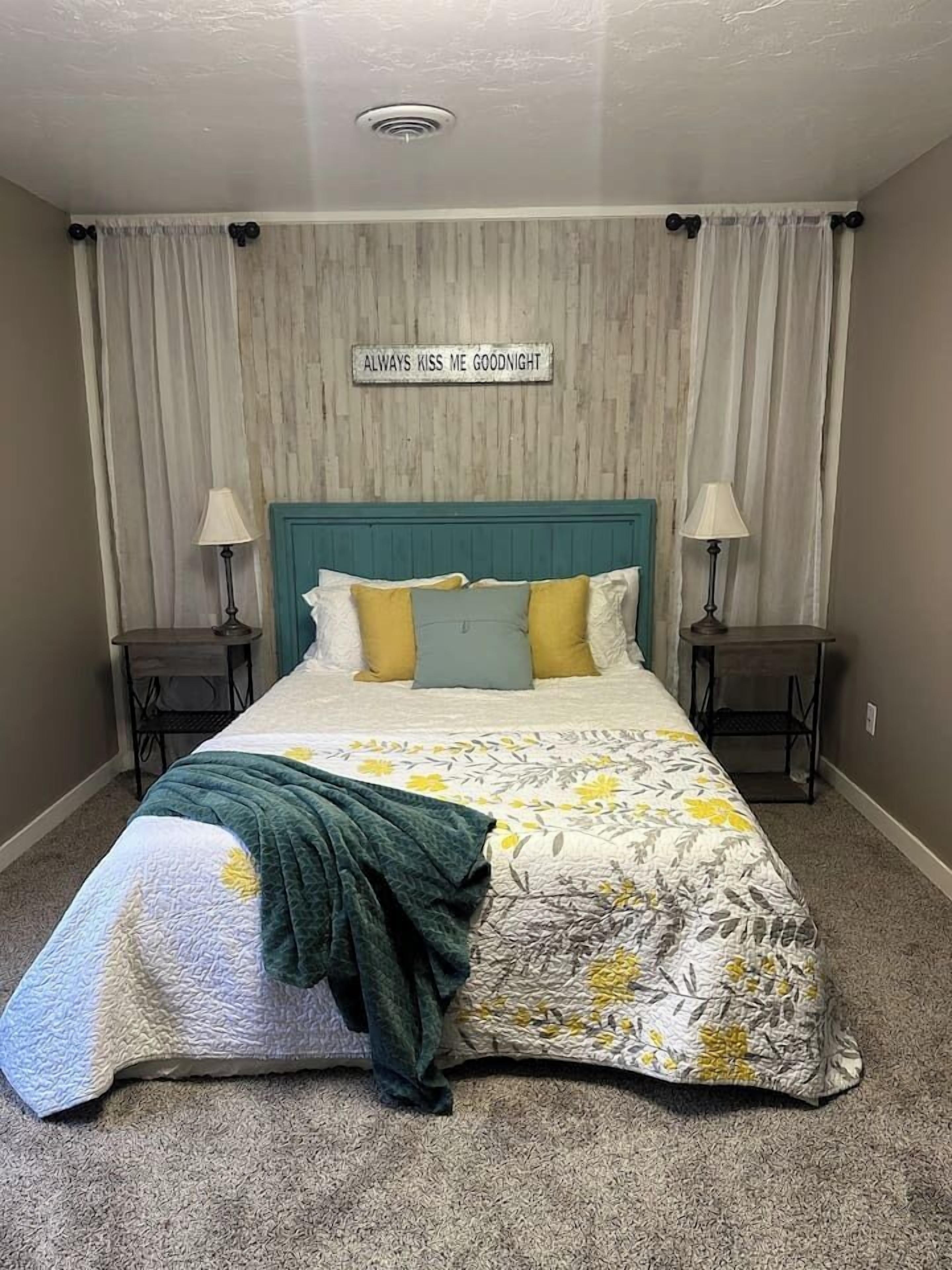 Un dormitorio con una cama, dos mesitas de noche, un cabecero y un cartel en la pared.