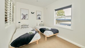 Une chambre avec deux lits simples, une fenêtre donnant sur un beau paysage et des œuvres d’art accrochées au mur.