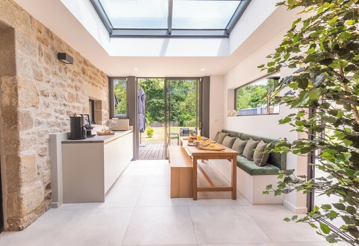 Una cocina moderna con pared de piedra, un área de comedor con banco y un amplio ventanal con vistas a un jardín.