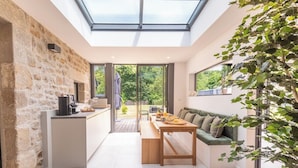 Una cocina moderna con pared de piedra, un área de comedor con banco y un amplio ventanal con vistas a un jardín.