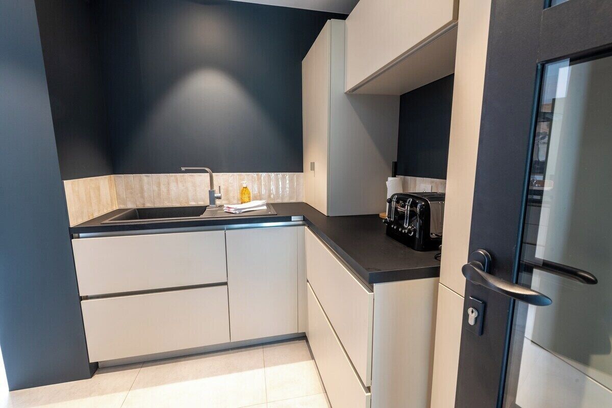 Et moderne køkken med hvide skabe, en sort bordplade og et stålskab.