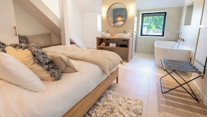 Un dormitorio con cama, ventana, baño con bañera y tragaluz.