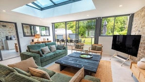 Un salón amplio con un televisor grande, sofás verdes y una zona de comedor con asientos exteriores.
