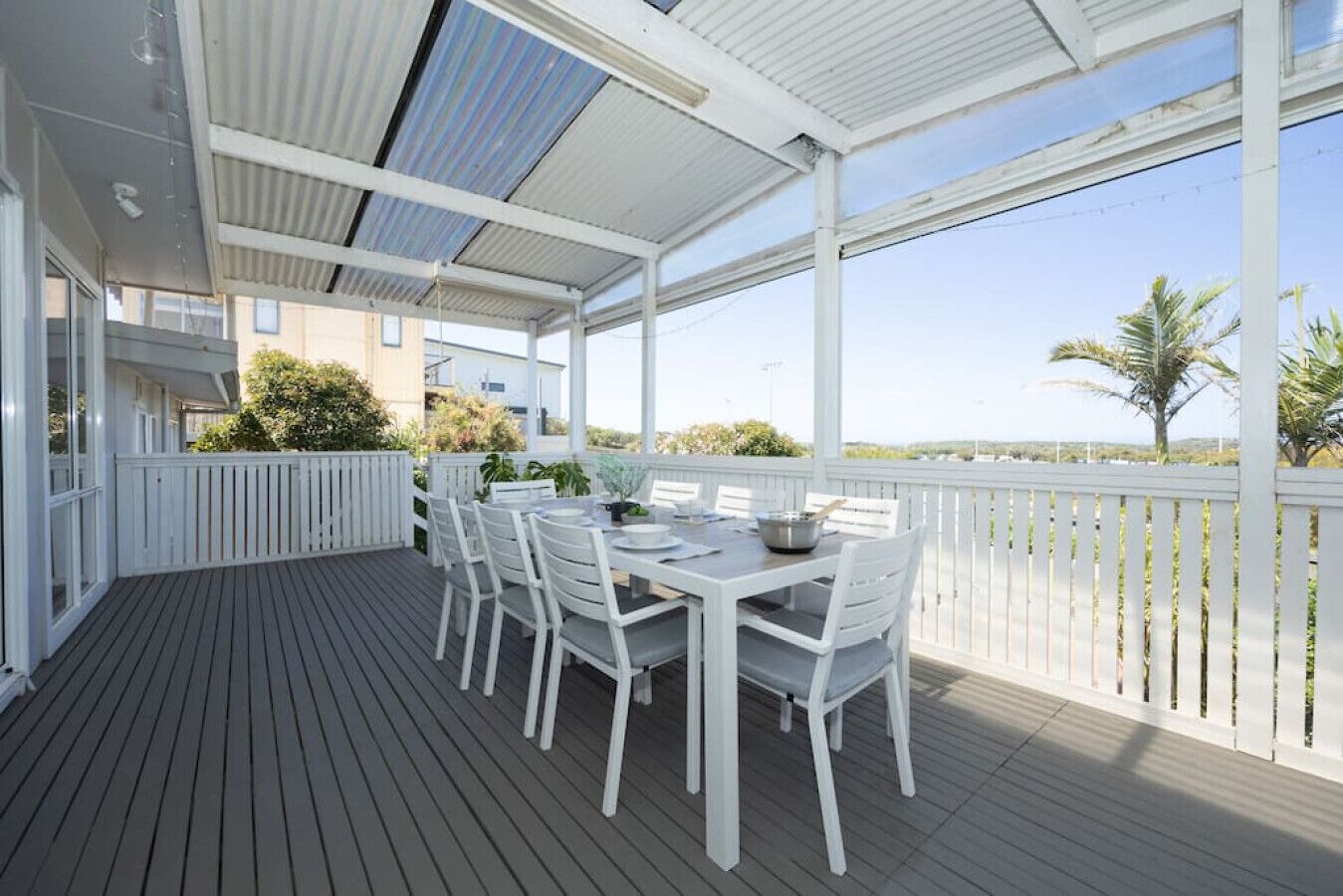 Un espace extérieur abrité, aménagé pour les repas, avec une terrasse en bois, des chaises blanches et une table dressée pour deux personnes.