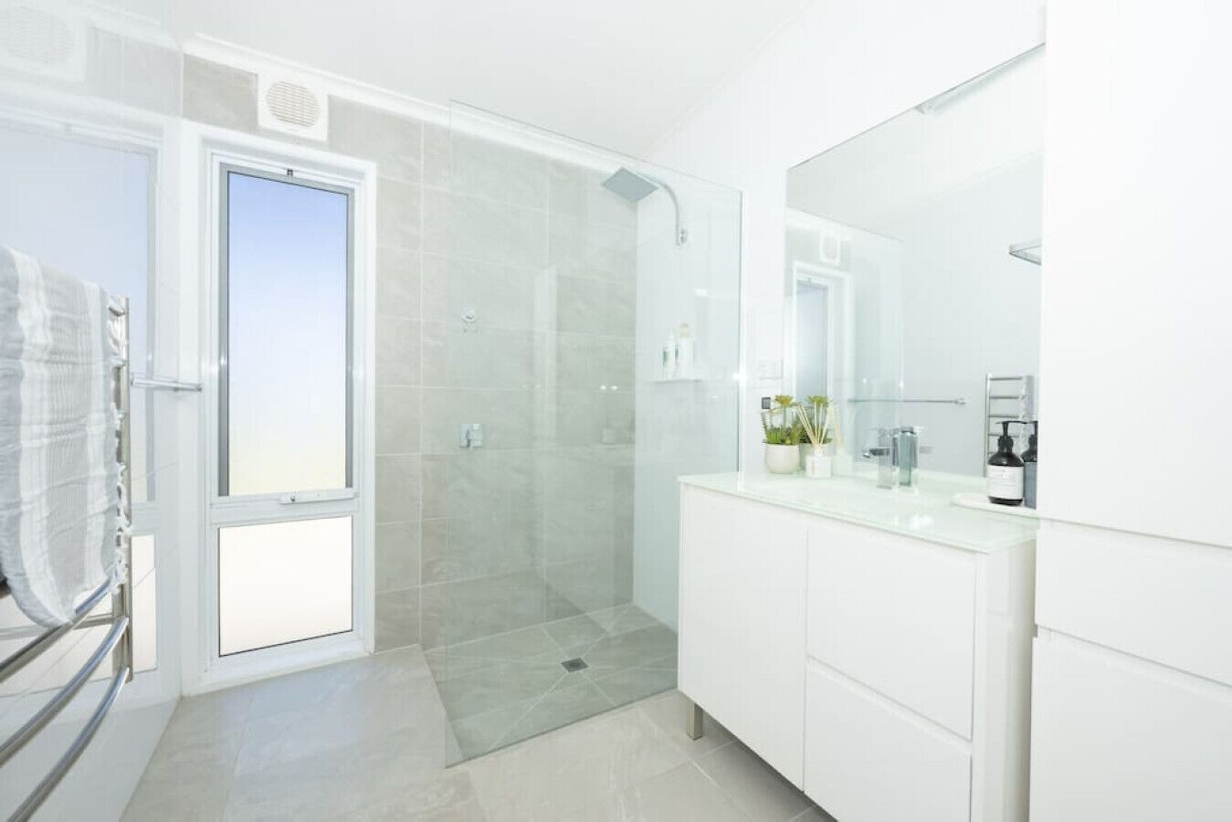 Une salle de bain moderne avec une douche à l’italienne en verre, un grand miroir et un meuble-lavabo blanc.