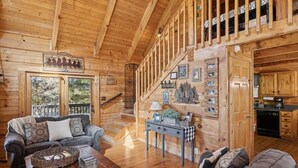 A wooden cabin interior with a staircase, a living room with a sofa and coffee table, and a kitchen area. - Firefly Holler by Beyond Expectations: Dog Friendly 3BR Cabin w/ EV Charger (Pigeon Forge)