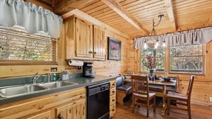 A wooden cabin interior with a kitchen, dining area, and a large window with a view. - Firefly Holler by Beyond Expectations: Dog Friendly 3BR Cabin w/ EV Charger (Pigeon Forge)