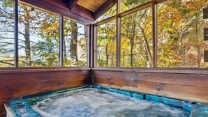 A hot tub with a view of autumn trees through large windows. - Firefly Holler by Beyond Expectations: Dog Friendly 3BR Cabin w/ EV Charger (Pigeon Forge)