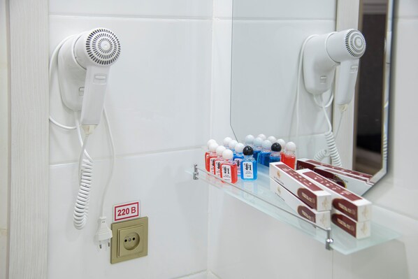 A bathroom with a hairdryer mounted on the wall, a shelf with various toiletries, and a mirror reflecting the hairdryer. - Art Home Hotel (Tashkent)