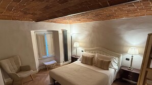 A bedroom with a large bed, two bedside tables with lamps, a chair, a window, and a brick ceiling. - Tuscan accommodation (20 minutes from Florence) (Prato)