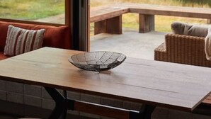 A modern dining area with a wooden table, red cushioned seating, and a view of a garden and pond.