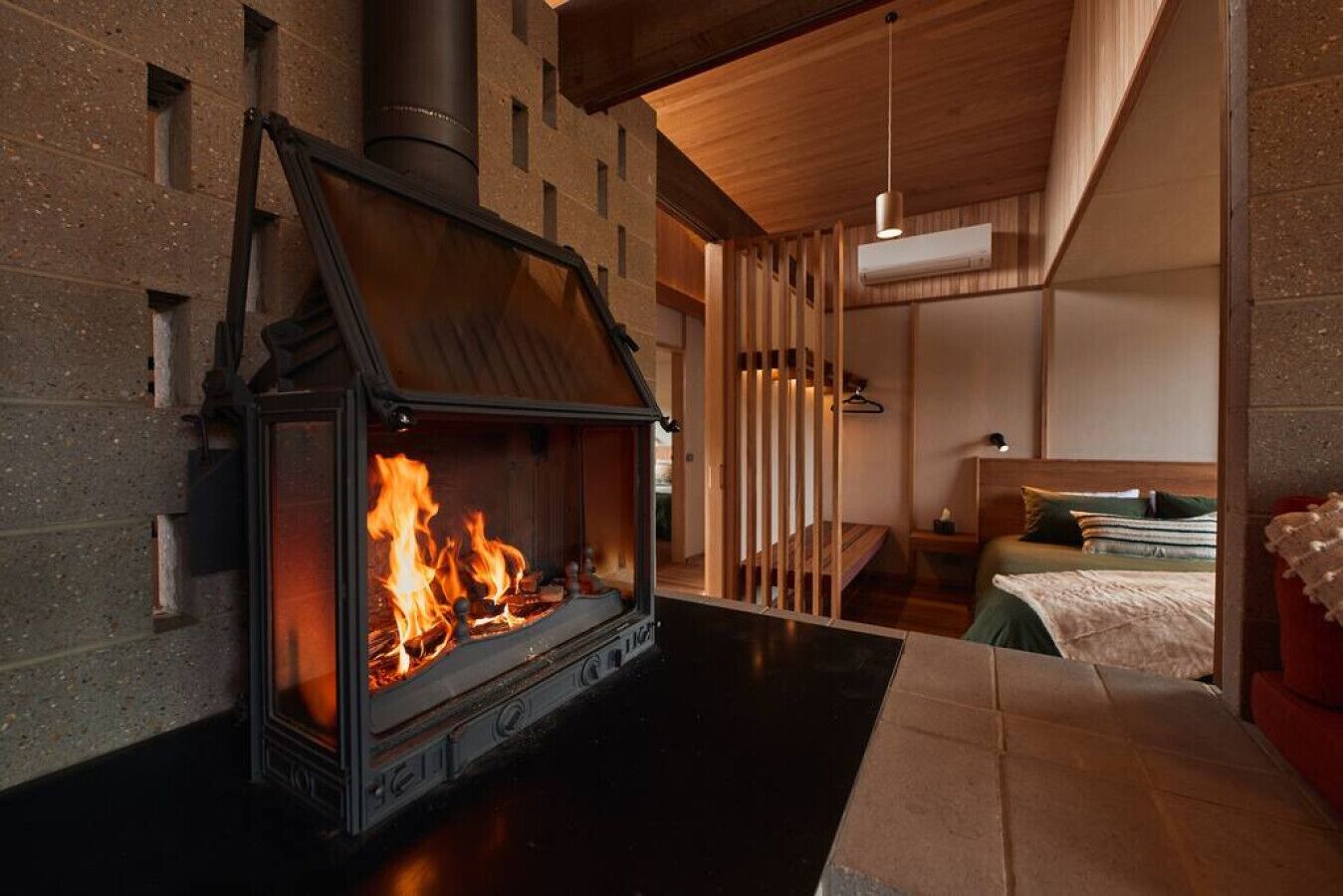 Un intérieur moderne avec un poêle à bois, un lit et un luminaire suspendu.