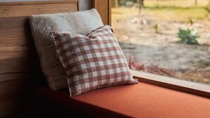 A window seat with a checkered pillow and a plain pillow.