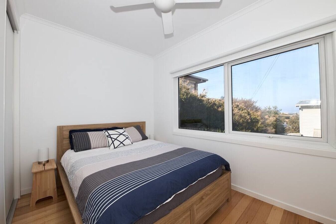 A bedroom with a bed, a nightstand, a window, and a ceiling fan.