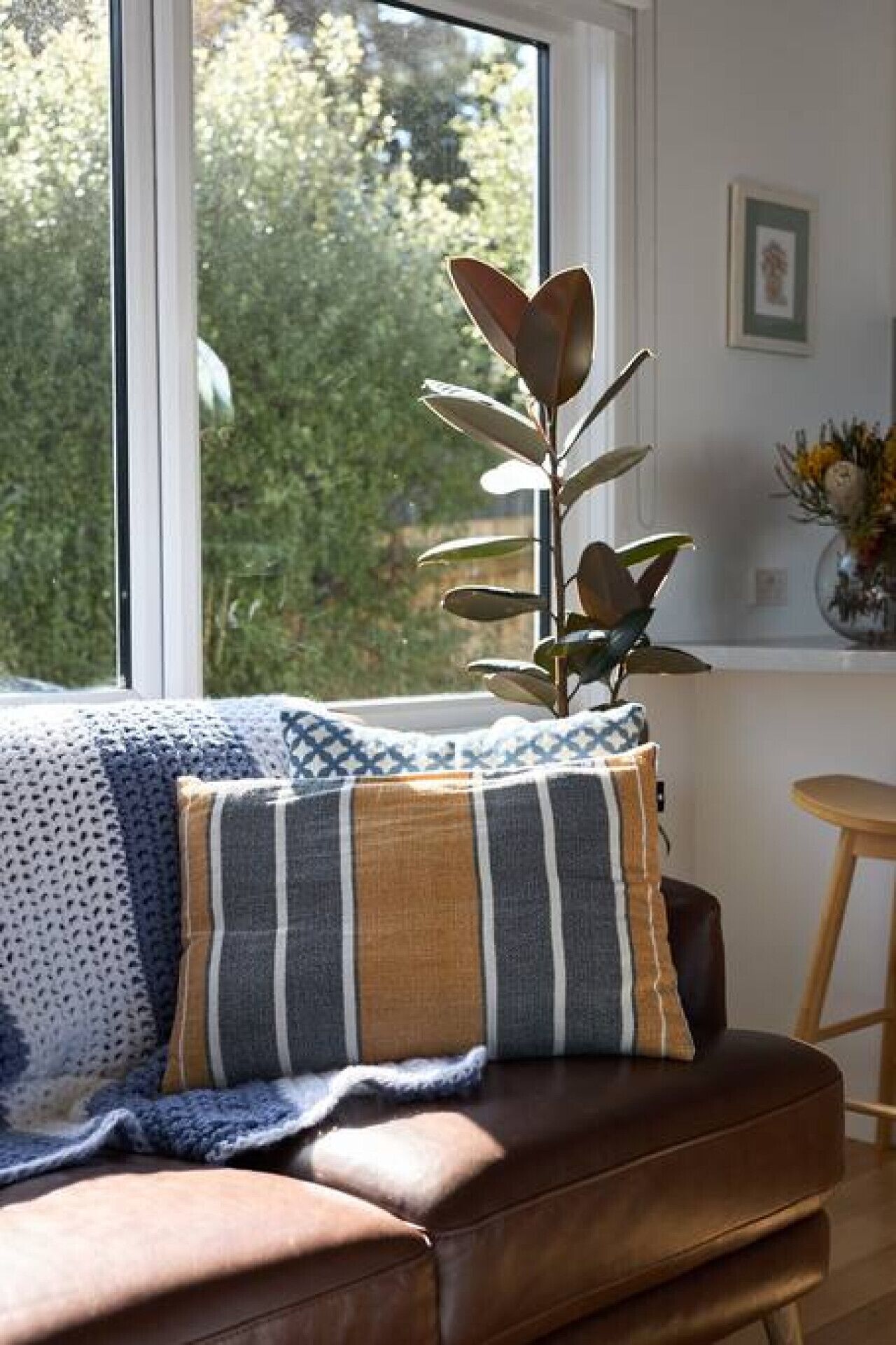A brown leather sofa with a striped pillow and a blue knitted blanket.