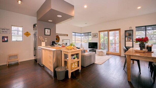 Amplia sala de estar con cocina, mesa de comedor y un gran ventanal que proporciona luz natural.