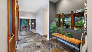 A spacious hallway with a stone floor, a wooden bench, and large windows with tropical plants. - Kurraburra Lodge (Anglesea)