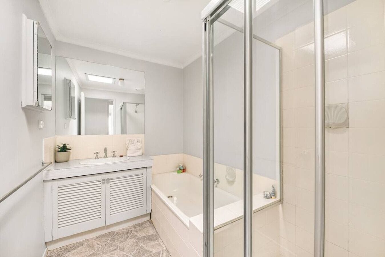 A modern bathroom with a glass shower enclosure, a freestanding bathtub, and a vanity with a mirror and sink.