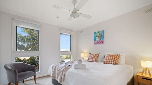 A bedroom with a bed, a chair, a ceiling fan, and a painting on the wall. - Secluded Anderson - in the heart of Torquay (Torquay)