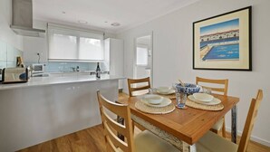 A modern kitchen with white cabinets, a wooden dining table set with plates and bowls, and a framed picture on the wall. - Secluded Anderson - in the heart of Torquay (Torquay)