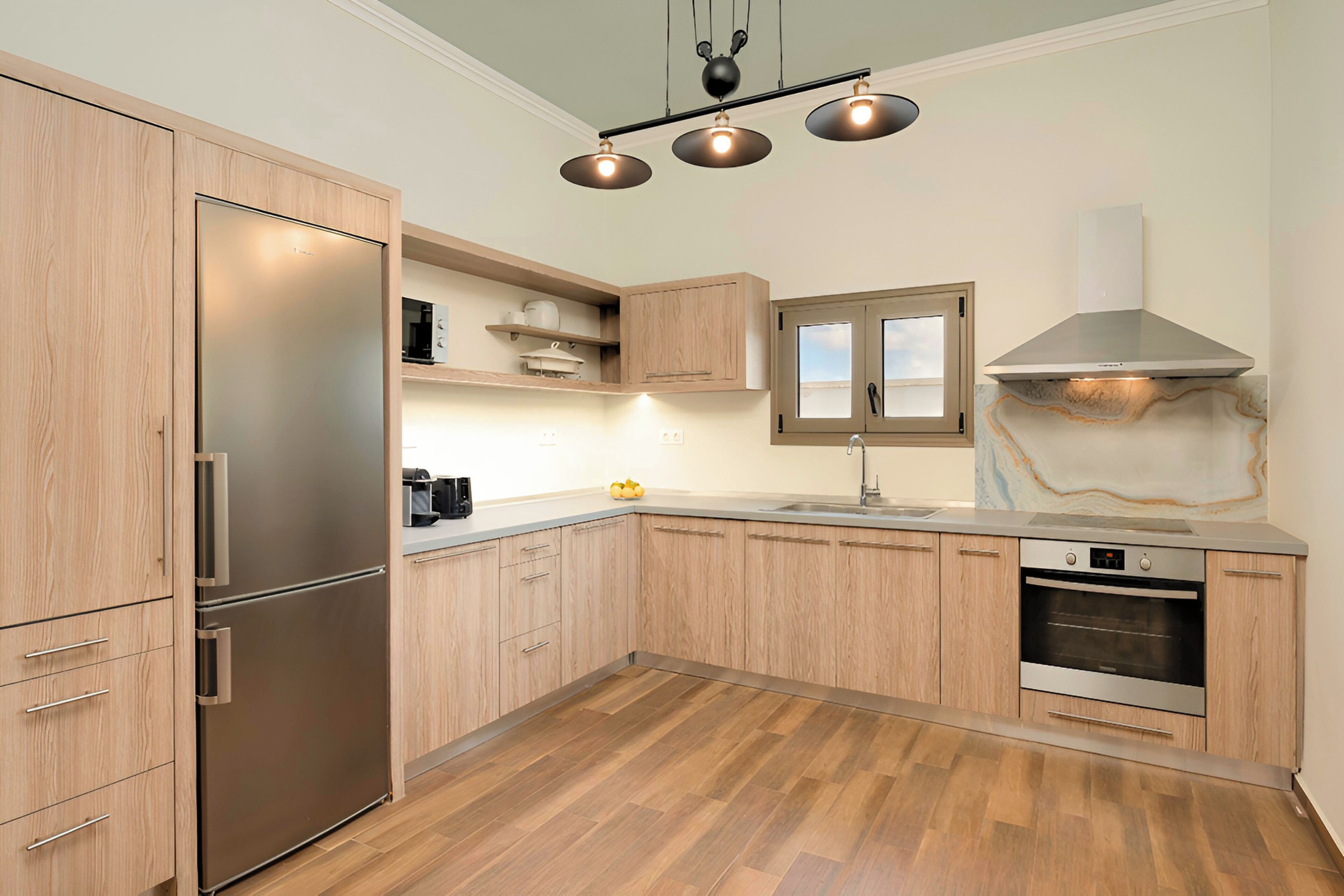 A modern kitchen with wooden cabinets, a stainless steel refrigerator, a built-in oven, and pendant lighting.