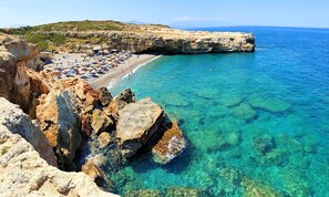 A coastal beach with clear turquoise waters, rocky cliffs, and a sandy beach area with umbrellas and sun loungers. - Villa di Capaka Private Pool (Roupes)