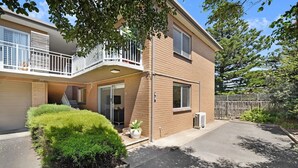 A two-story residential building with a balcony, a covered entryway, and a small front yard with a bush. - Cosy living at Cosy corner (Torquay)