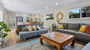 A modern living room with a grey sofa, wooden coffee table, and a kitchen in the background. - Barwon Bliss - Ocean Grove (Ocean Grove)