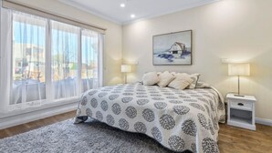 A bedroom with a large bed, a painting on the wall, and a window with curtains. - Barwon Bliss - Ocean Grove (Ocean Grove)