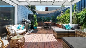 A covered patio with wooden flooring, wicker furniture, a grill, and potted plants. - Barwon Bliss - Ocean Grove (Ocean Grove)
