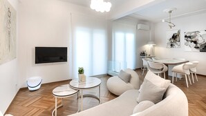 Un salon moderne avec un canapé, deux petites tables, un téléviseur et des œuvres d’art accrochées aux murs.