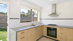 A kitchen with a gas stove, oven, and a window overlooking a backyard. - Beach Breeze Bungalow - in the heart of Torquay (Torquay)