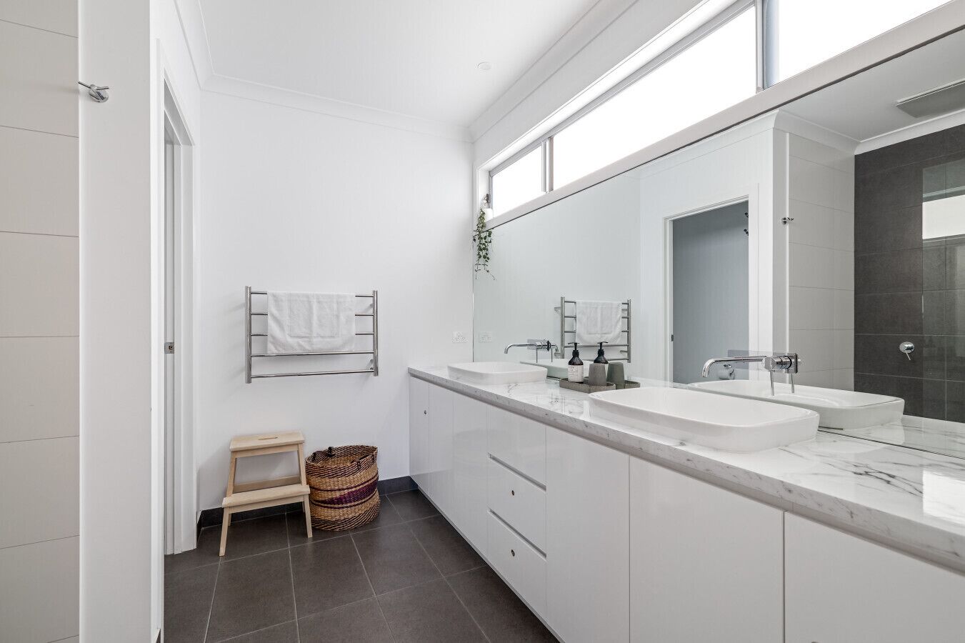 Une salle de bain moderne avec deux lavabos, un grand miroir et un petit tabouret en bois.