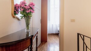 Un pasillo con un aparador de madera, un florero de flores rosadas y un espejo en la pared.