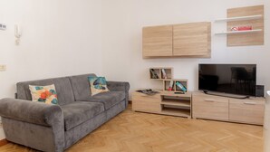 Una sala de estar moderna con un sofá gris, armarios de madera, un televisor de pantalla plana y un piso con estampado tipo espiga.