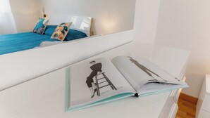 Una habitación con una cama, un aparador blanco y un libro abierto sobre él.