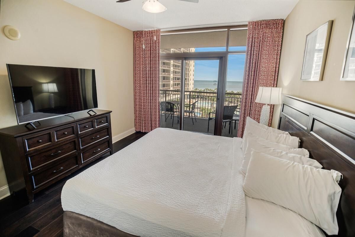 Une chambre d’hôtel avec un grand lit, une télévision, une commode et un balcon donnant sur l’océan.