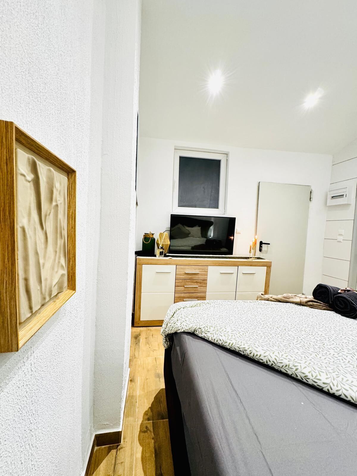 A bedroom with a bed, a TV, a dresser, and a mirror.