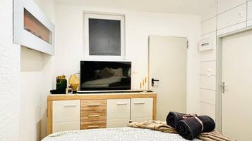 A bedroom with a bed, a TV on a wooden dresser, a framed picture, and a mirror.