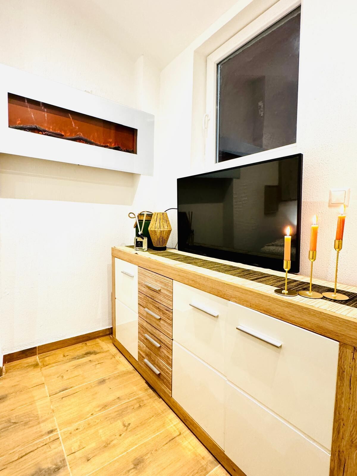 A modern kitchen with a wooden countertop, white cabinets, a large window, and a flat-screen TV.