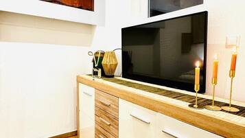 A modern kitchen with a wooden countertop, white cabinets, a large window, and a flat-screen TV.