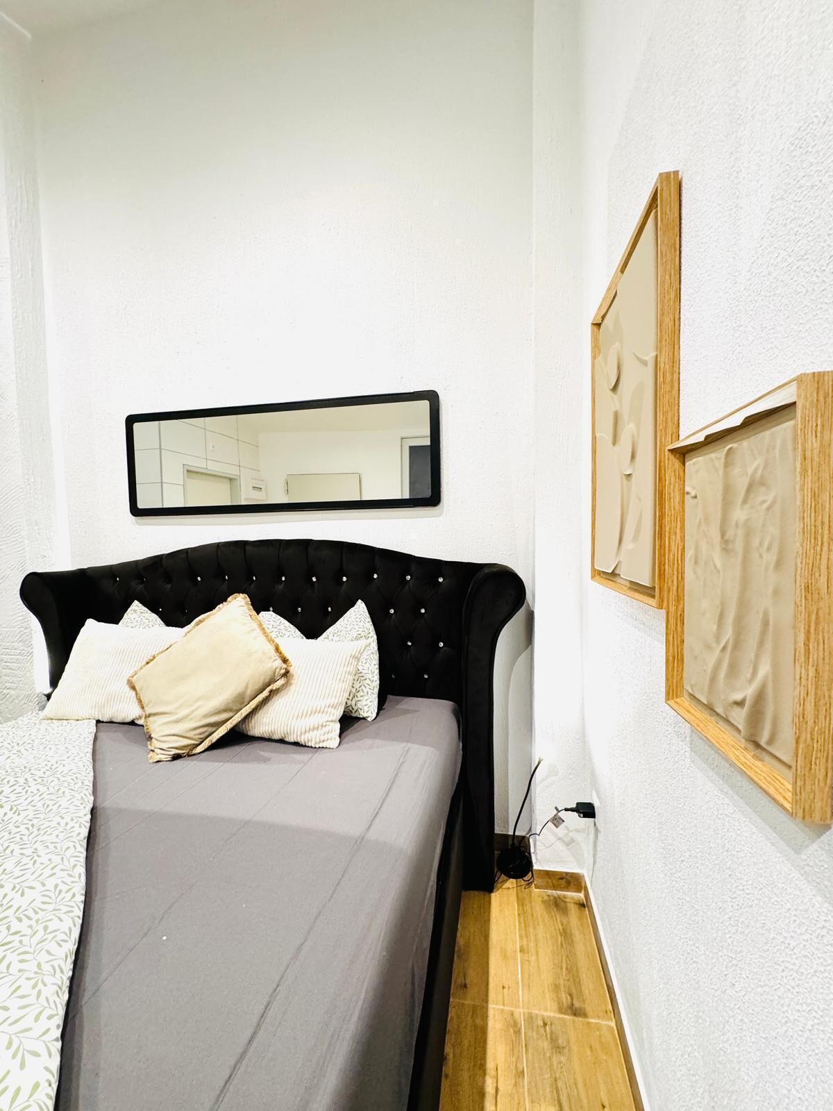 Une chambre à coucher avec un lit, un miroir et deux tableaux encadrés accrochés au mur.